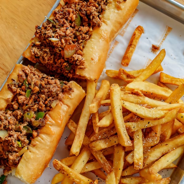 Two chicken cheesesteak sandwiches with green peppers and onions, served with a side of fries.