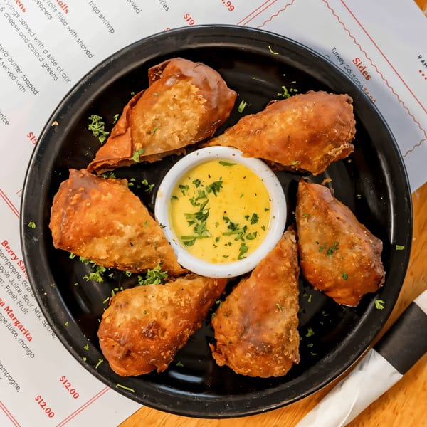 Six crispy fried Sunrise Social breakfast egg rolls arranged around a small bowl of yellow dipping sauce.