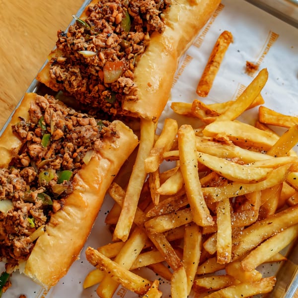 Two hearty breakfast cheesesteak sandwiches with peppers and onions, served with a side of seasoned fries.
