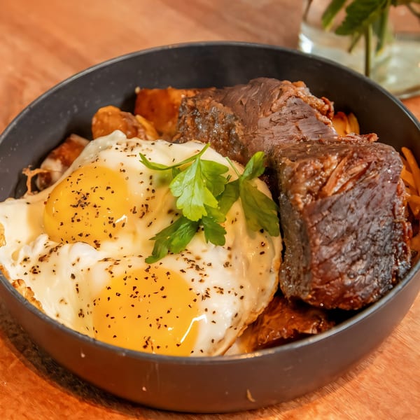 Sunrise Social's breakfast bowl with braised short rib, crispy potatoes, fried eggs, and fresh parsley.