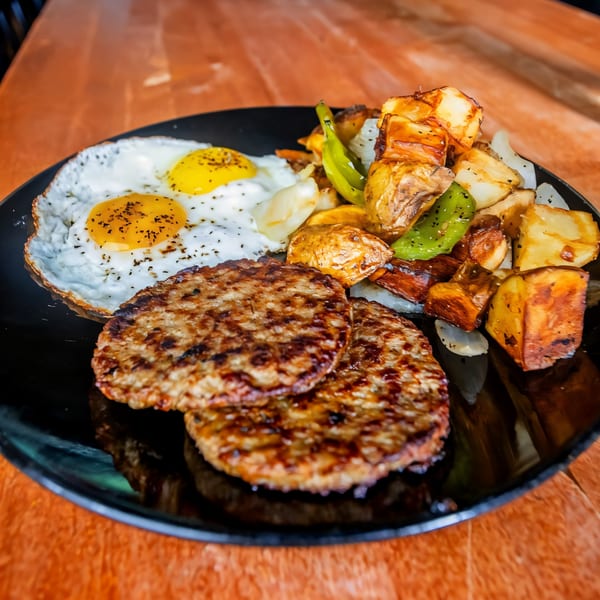 Sunrise Social breakfast plate with two fried eggs, sausage patties, and roasted potatoes with peppers.