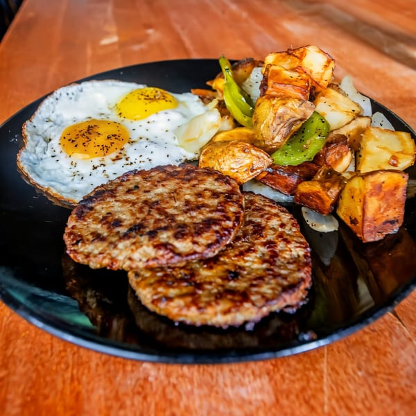 Sunrise Social's breakfast plate with two fried eggs, sausage patties, and roasted potatoes with peppers.