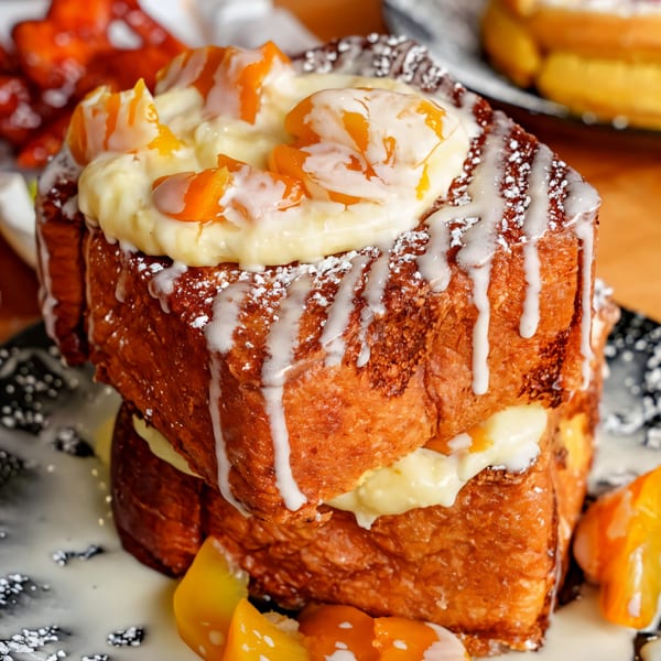 Stacked French toast with creamy topping, peaches, powdered sugar, and glaze at Sunrise Social.