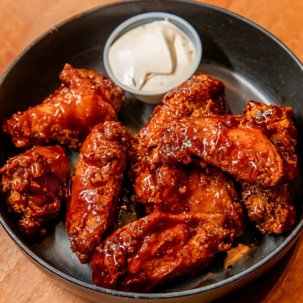 A black bowl filled with glazed chicken wings and a side of creamy dipping sauce.